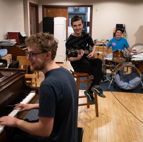 Three students play drums, guitar, and piano in the Maple Tree Studio.